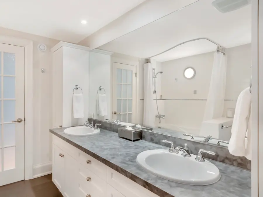 Baño renovado con lavamanos doble, mesón de piedra y muebles blancos